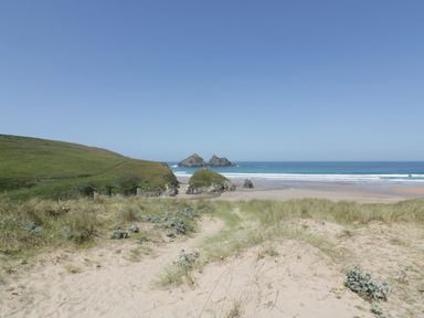A sandy beach with dunes and grass leading to the ocean with rock formations in the water at Atlantic View in Holywell Bay
