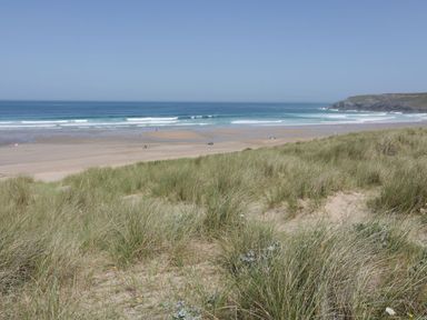A sandy beach with grassy dunes and people near the water at Atlantic View in Holywell Bay