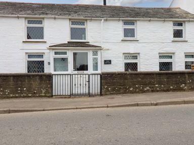 The exterior of a white brick cottage with multiple windows and a gated front entrance at Crab Cottage in Delabole