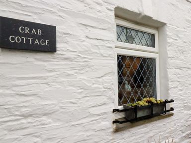 A white textured wall with a window featuring diamond-shaped panes and a flower box below it at Crab Cottage in Delabole