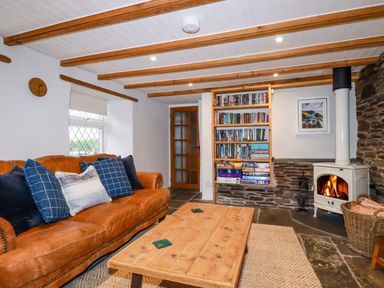 A living room with a leather sofa blue cushions wooden coffee table bookshelf and a wood burning stove at Crab Cottage in Delabole