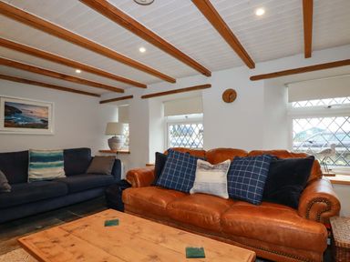A living room with leather and fabric sofas wooden beams on ceiling and a wooden coffee table at Crab Cottage in Delabole