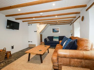 A living room with sofas a wooden coffee table a wall mounted television and exposed wooden ceiling beams at Crab Cottage in Delabole