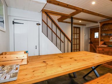 A dining area with a wooden table and bench under stairs with a wooden door and cupboard at Crab Cottage in Delabole