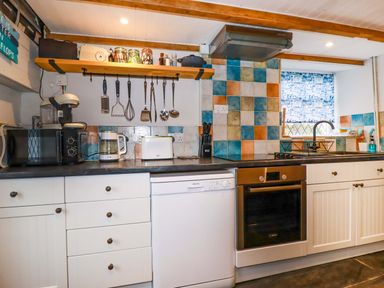 A kitchen with white cabinets black countertop and colorful tiled backsplash at Crab Cottage in Delabole