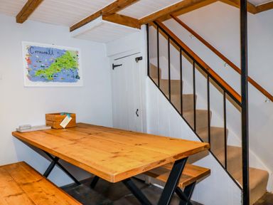 A wooden dining table with benches next to a staircase and a framed map on the wall at Crab Cottage in Delabole
