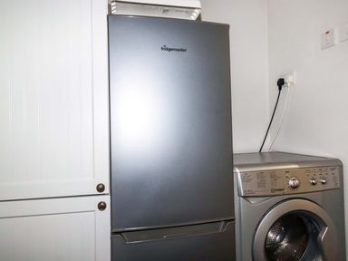 A silver fridge next to a silver front-loading washing machine in a utility room at Crab Cottage in Delabole