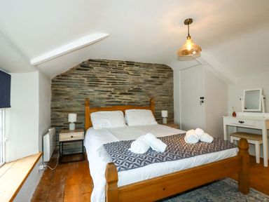 A bedroom with a wooden double bed and bedside tables under a sloped ceiling at Crab Cottage in Delabole