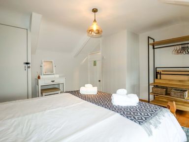 A bedroom with a bed folded towels a white dressing table with a mirror and an open wooden shelving unit at Crab Cottage Delabole