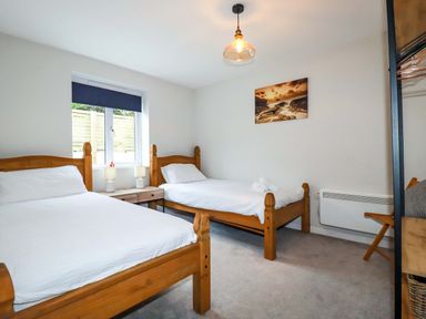 A bedroom with two wooden single beds a window with a blind a small bedside table with lamps and a chair at Crab Cottage in Delabole