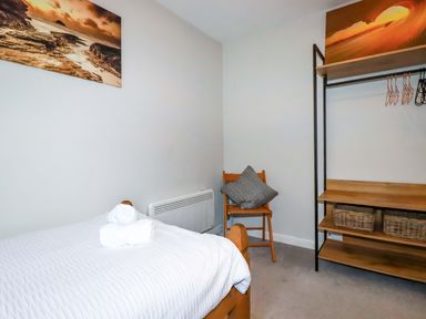 A bedroom with a single bed with white bedding a wooden chair with pillows and an open wardrobe with baskets at Crab Cottage in Delabole