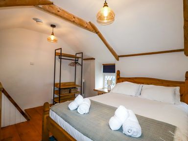 A bedroom with a wood bed and a rack with hangers and baskets at Crab Cottage in Delabole