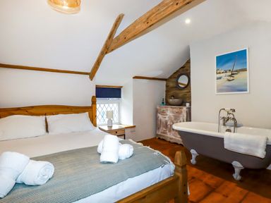 A bedroom with a wooden bed and nightstand next to a window and a bathtub and washbasin at Crab Cottage in Delabole