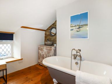 A bathroom with a clawfoot bathtub a wooden vanity with a stone sink a small window and a framed picture of boats at Crab Cottage in Delabole