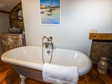 A bathroom with a freestanding bathtub a towel wooden cabinetry with stone sink and a painting at Crab Cottage in Delabole