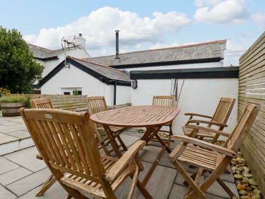 An outdoor patio with wooden table and six chairs next to a white building at Crab Cottage in Delabole