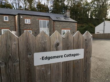 A wooden fence with a sign that says Edgemere Cottages and stone cottages in the background at Edgemere Cottage in Cartmel