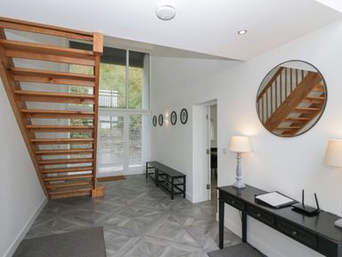 An entryway with wooden stairs glass doors a black console table with lamps and a round mirror at Edgemere Cottage in Cartmel