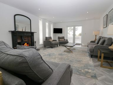 A living room with gray sofas a fireplace a coffee table and a wall-mounted tv at Edgemere Cottage in Cartmel