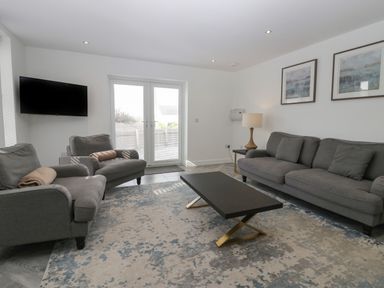 A living room with gray sofas a black coffee table a wall-mounted TV and two framed pictures at Edgemere Cottage in Cartmel