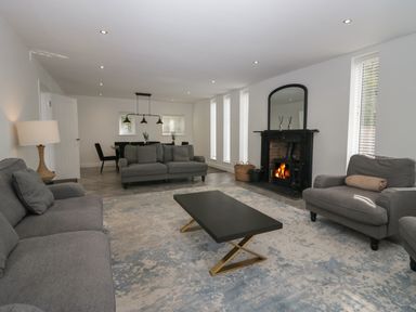 A living room with grey sofas a black coffee table a fireplace and a dining area at Edgemere Cottage in Cartmel