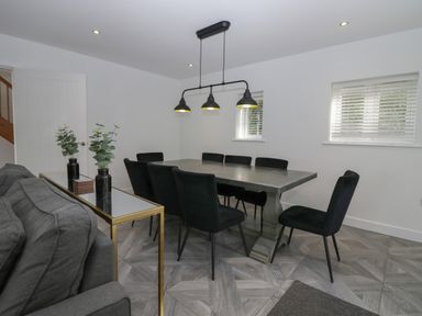 A dining room with a large table and black chairs and a gray sofa and two vases with plants at Edgemere Cottage in Cartmel