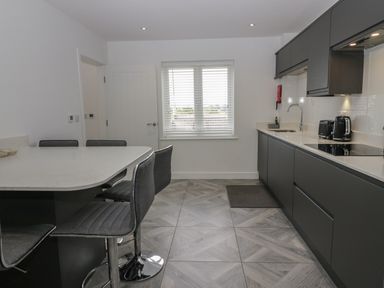 A kitchen with a countertop breakfast bar and bar stools and dark cabinets at Edgemere Cottage in Cartmel