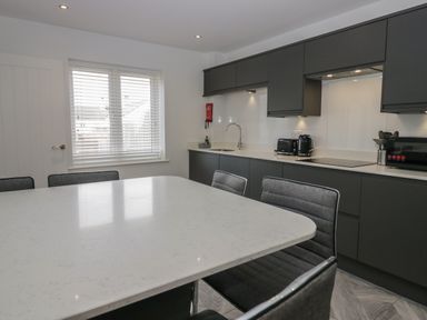 A kitchen with a white countertop island and grey chairs near cabinets with a sink toaster kettle and microwave at Edgemere Cottage in Cartmel