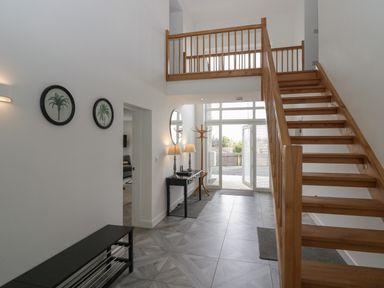 Hallway with wooden staircase a black bench two framed pictures table with two lamps and a mirror at Edgemere Cottage in Cartmel