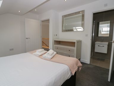 A bedroom with a bed and folded towels a dresser with a mirror and an en suite bathroom at Edgemere Cottage in Cartmel