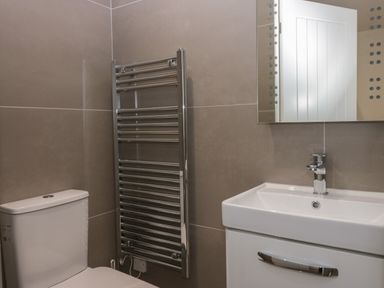 A bathroom with a toilet a heated towel rail a sink with a faucet and a mirror at Edgemere Cottage in Cartmel