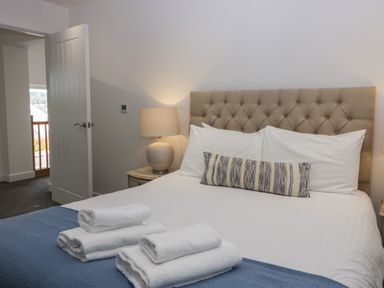 A bedroom with a made bed with white sheets and pillows a blue throw and folded towels beside a nightstand with a lamp at Edgemere Cottage in Cartmel