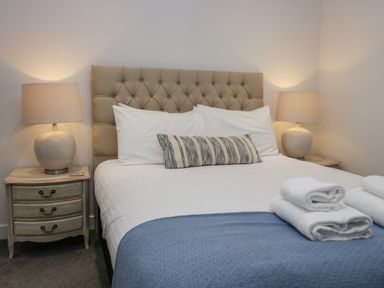 A bedroom with a bed with white linens and a blue throw blanket with folded towels on top and two bedside tables with lamps at Edgemere Cottage in Cartmel