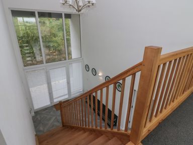 A wooden staircase leading down to a landing with large windows and a wall with framed pictures and a bench at Edgemere Cottage in Cartmel