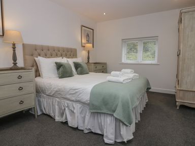 A bedroom with a double bed with green pillows and white linens two bedside tables with lamps a window and a wardrobe at Edgemere Cottage in Cartmel