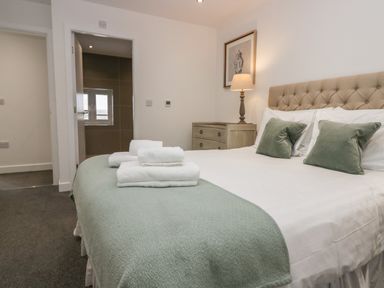 A bedroom with a bed with green pillows and folded towels on the bed with a bedside table and lamp at Edgemere Cottage in Cartmel
