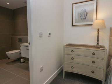 A bedroom corner with a dresser and lamp next to a bathroom with a toilet and sink at Edgemere Cottage in Cartmel
