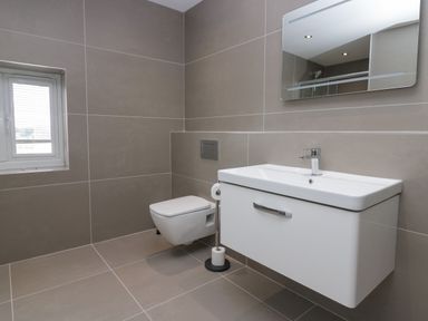 A bathroom with a wall-mounted toilet a sink with cabinet and mirror at Edgemere Cottage in Cartmel