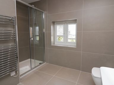 A bathroom with a shower enclosure a window and a towel radiator at Edgemere Cottage in Cartmel