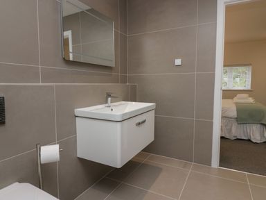 A bathroom with a wall-mounted sink and mirror next to a bedroom at Edgemere Cottage in Cartmel