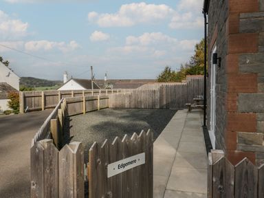 A fenced outdoor area with a gate and a sign reading Edgemere beside a stone building at Edgemere Cottage in Cartmel