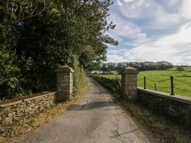 A country road passing between stone pillars with green fields on one side and trees on the other at Edgemere Cottage in Cartmel