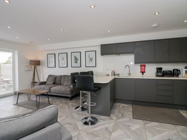 A kitchen and living area with a gray sofa wooden coffee table bar stools and framed plant pictures at Edgemere Retreat in Cartmel