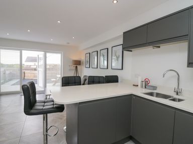 A kitchen and dining area with bar stools pictures on the wall and sliding glass doors at Edgemere Retreat in Cartmel