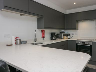 A modern kitchen with grey cabinets a white countertop a sink coffee maker microwave and oven at Edgemere Retreat in Cartmel