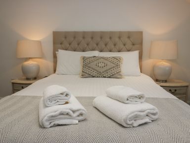 A bed with two bedside tables with lamps two sets of folded white towels and a decorative pillow at Edgemere Retreat in Cartmel