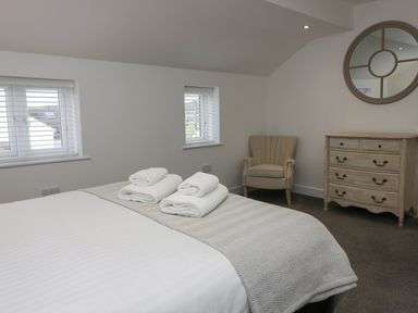 A bedroom with a bed with folded towels two windows an armchair a dresser and a round mirror at Edgemere Retreat in Cartmel