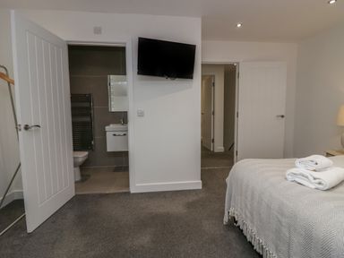 A bedroom with a bed with folded towels on it a wall-mounted tv and an open door to a bathroom at Edgemere Retreat in Cartmel