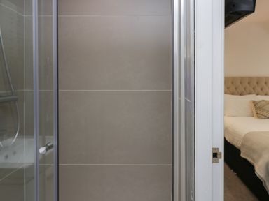 A bathroom with tiled walls and a glass shower door next to a bedroom with a bed at Edgemere Retreat in Cartmel