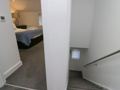 A hallway with stairs going down and a bedroom with a bed and lamp at Edgemere Retreat in Cartmel